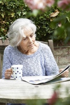 Senior Woman Relaxing In Garden Reading Newspaper