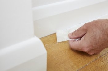 Close Up Of Man Removing Masking Tape From Skirting Board