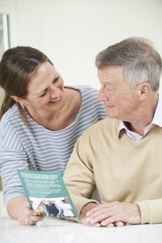 Senior Man With Adult Daughter Looking At Brochure For Retirement Home