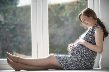 Pregnant Woman Relaxing By Window At Home