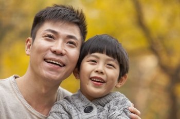 Father and son smiling in the park in autumn, close-up portrait