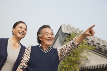 Happy senior couple outdoors pointing by traditional building in Beijing