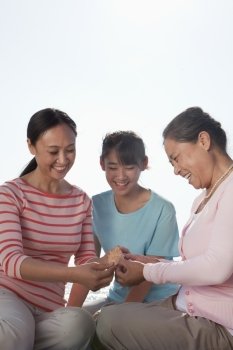 Three generations looking at seashell, China