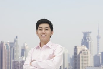 Portrait of young businessman in button down shirt with arms crossed, Shanghai skyline 