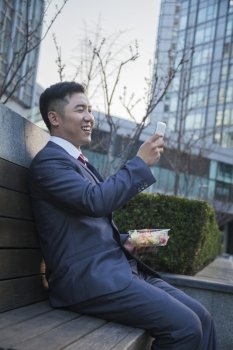 Smiling businessman on lunch texting on his mobile phone outdoors