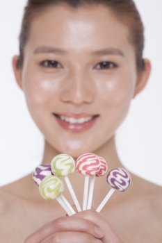 Smiling young woman looking into camera and holding up colorful lollipops, studio shot