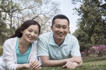 Portrait of couple lying in grass in park.