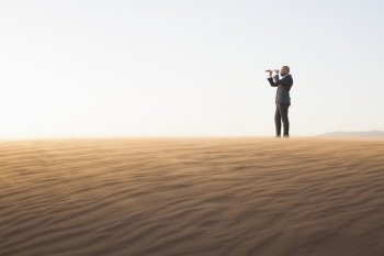 Young businessman looking through telescope in  the middle of the desert