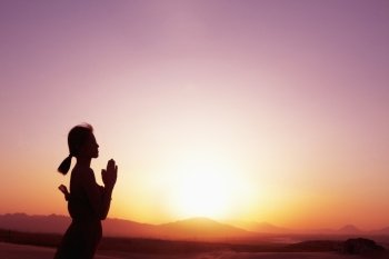 Serene young woman with hands together in prayer pose  in the desert in China, silhouette, profile, sun setting