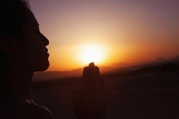 Serene young woman with hands together in prayer pose  in the desert in China, silhouette, sun setting