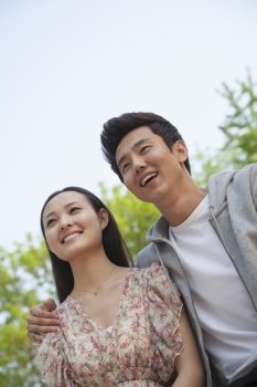 Smiling happy young couple with arm around the shoulders outdoors in a park, front view
