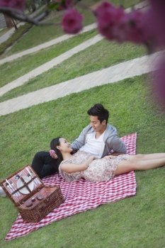 Young happy couple lying on a blanket together while having a picnic in the park, blossoms in the foreground