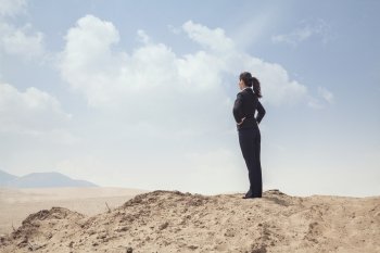Young businesswoman standing with hands on hips looking out over the desert