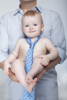 Portrait of smiling baby wearing only a tie and being carried by his father, studio shot