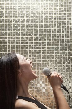 Side view of young woman singing into a microphone at karaoke, shiny background