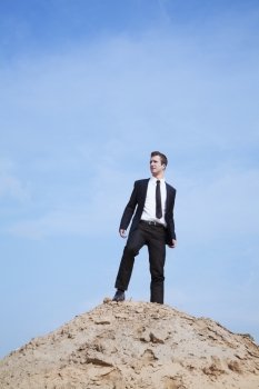 Young solitary businessman standing on a hill in the desert