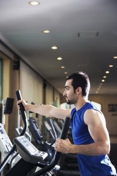 Young muscular man exercising on a cross trainer in the gym