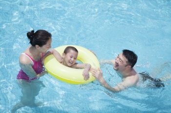Smiling happy family playing in the pool with their son in an inflatable tube