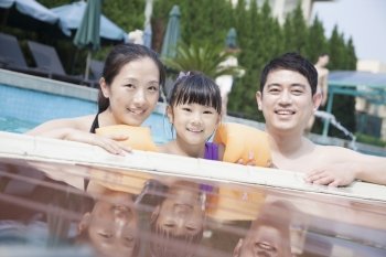 Portrait of smiling family in the pool by the edge looking at camera