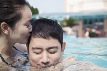Woman with eyes closed kissing man on the cheek in the water in the pool