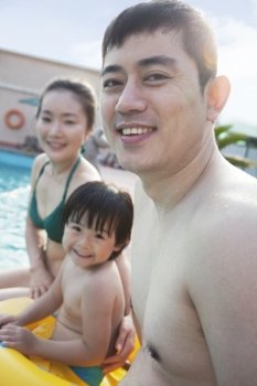 Portrait of smiling happy family sitting by the pool 