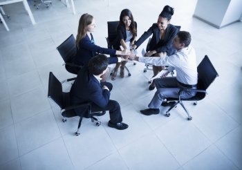 Business people sitting in a circle with hands together cheering