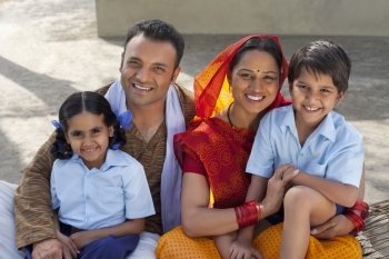 Portrait of a happy Indian family of four sitting on cot 