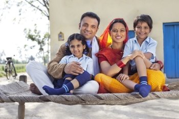 Portrait of happy rural Indian family sitting on cot 