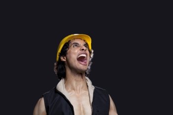 Close-up of young man with hardhat shouting against black background 