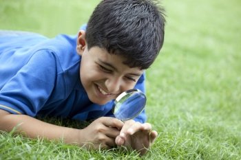 Boy lying on grass using magnifying glass 