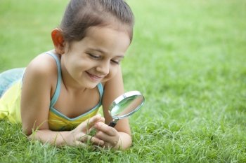 Cute little girl looking through magnifying glass in the park 