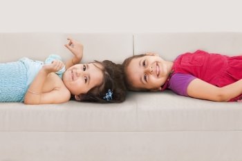 Cute little sisters lying on sofa 