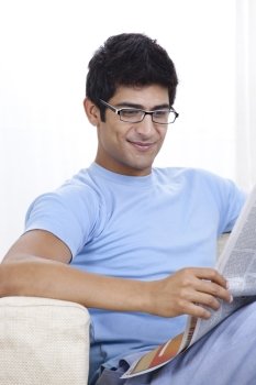 Happy young Indian man reading newspaper at home 