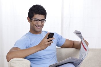 Happy young man looking at mobile phone while sitting on sofa 