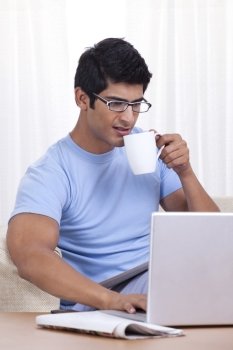 Young man taking a sip of coffee while operating laptop 