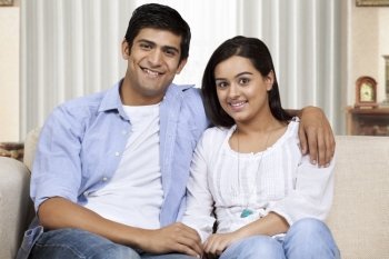 Happy young couple with arm around sitting on sofa 
