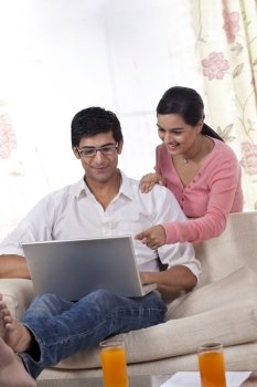 Young woman pointing at laptop while man using laptop 