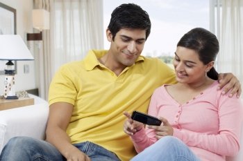 Young couple using cell phone while sitting on sofa 