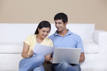 Young couple looking at document while using laptop 