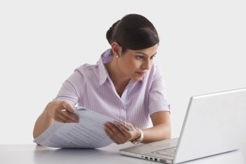 Businesswoman with paperwork looking at laptop screen 