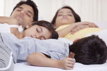 Family sleeping on bed 