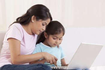 Woman helping her daughter to use a laptop 