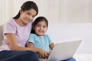Portrait of woman helping her daughter to use a laptop 