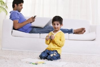 Boy holding felt tip pen with father using cell phone in the background 
