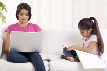Woman working on laptop while daughter drawing 