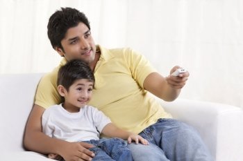 Smiling father changing channels while sitting with his son 