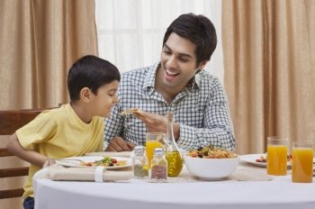 Happy father feeding piece of pizza to his son at restaurant 