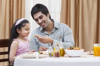 Happy father feeding his cute daughter a piece of pizza at restaurant 