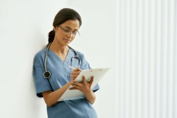 Young female surgeon writing notes while leaning on wall 
