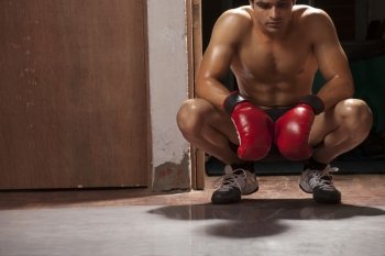 Tired male boxer crouching in gym